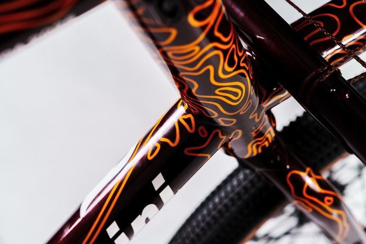Macro detail of a Tommasini frame with the orange Impanga topographic pattern over deep burgundy paint