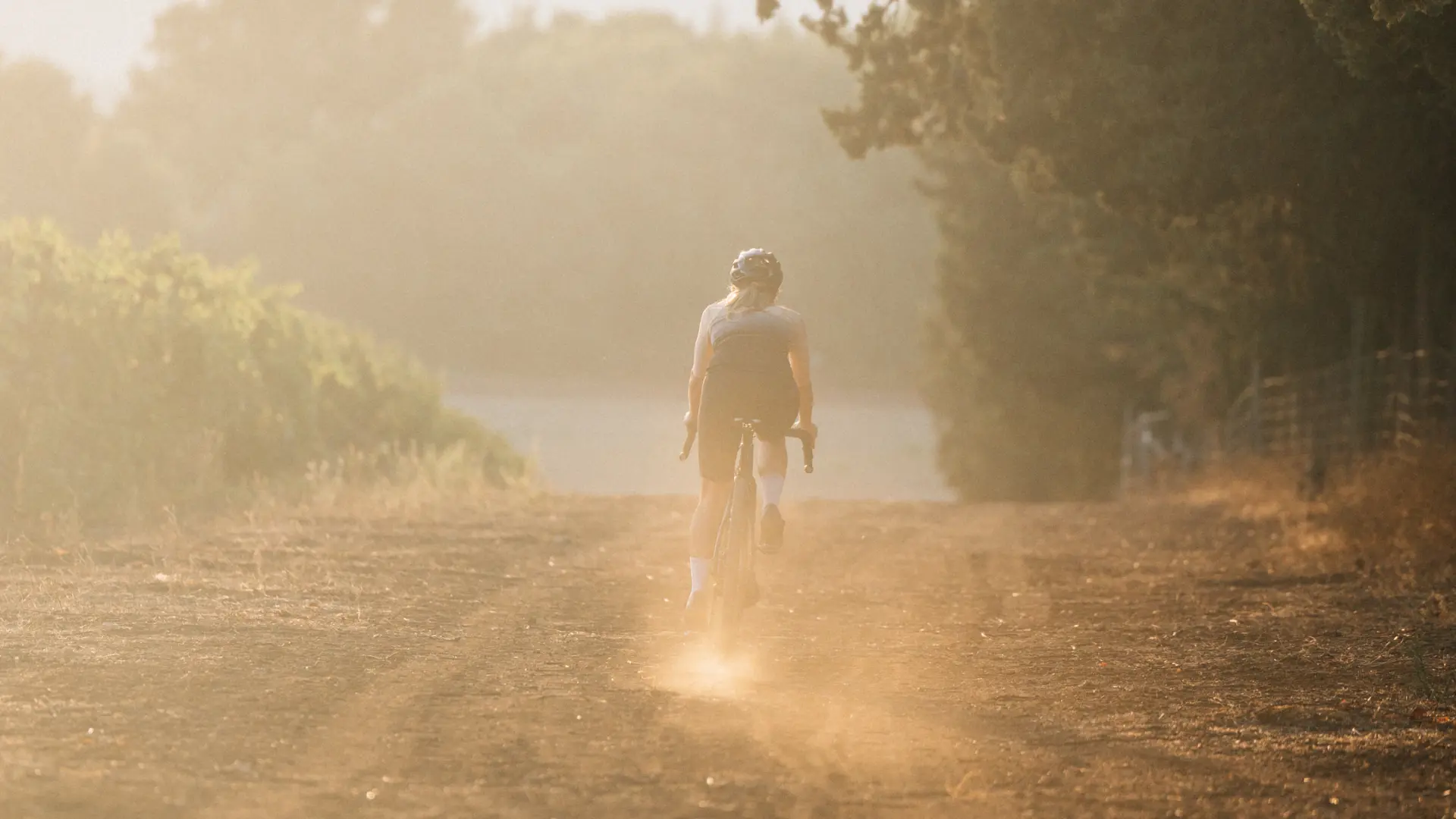 A rider disappearing into dust on a gravel road at sunrise