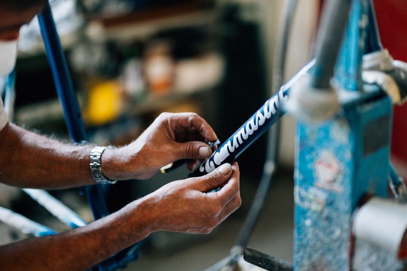 Artisan hand-painting the Tommasini signature on a blue steel frame